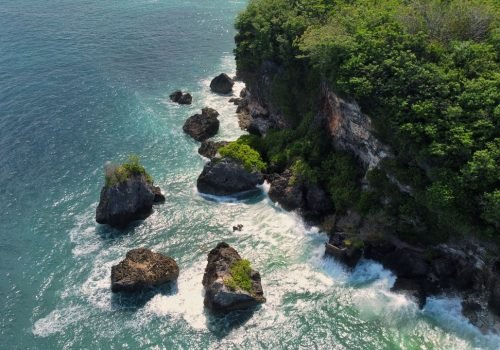 Stunning aerial view of a rocky coastline with lush greenery in Bali, Indonesia.