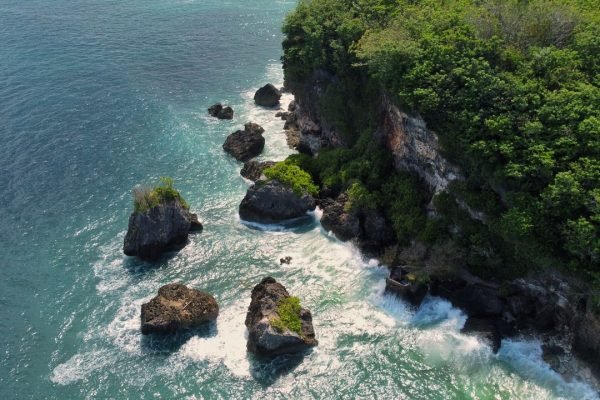 Stunning aerial view of a rocky coastline with lush greenery in Bali, Indonesia.